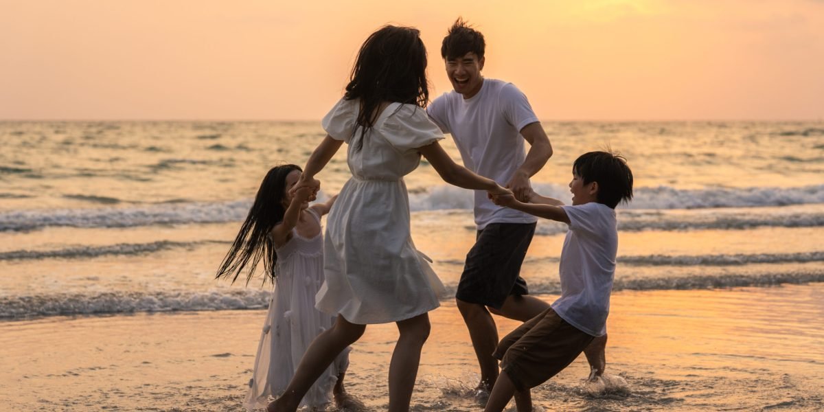 Asian young happy family enjoy vacation on beach in the evening. Dad, mom and kid relax playing together near sea when silhouette sunset. Lifestyle travel holiday vacation summer concept.