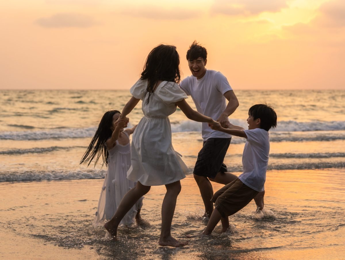 Asian young happy family enjoy vacation on beach in the evening. Dad, mom and kid relax playing together near sea when silhouette sunset. Lifestyle travel holiday vacation summer concept.